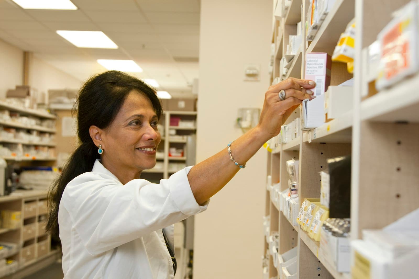 A pharmacist reaching for a medicine box on a dispensary shelf
